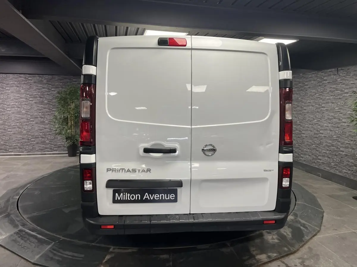 Vue arrière d'un utilitaire Nissan Primastar blanc avec portes battantes et feux verticaux rouges.