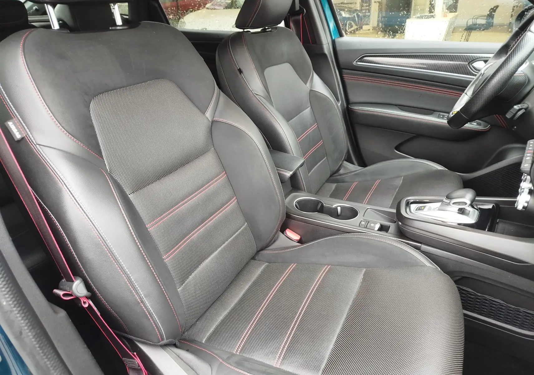 Vue intérieure côté conducteur du Renault Arkana 1.6 E-Tech bleu Zanzibar, sièges noirs avec surpiqûres rouges et console centrale.