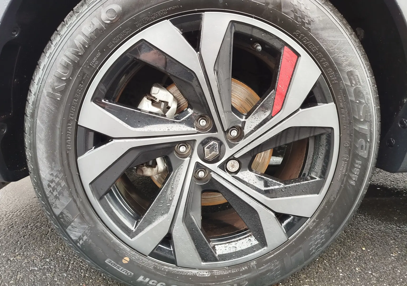 Gros plan sur la jante alliage noire et grise avec insert rouge du Renault Arkana bleu Zanzibar, roue avant droite mouillée.