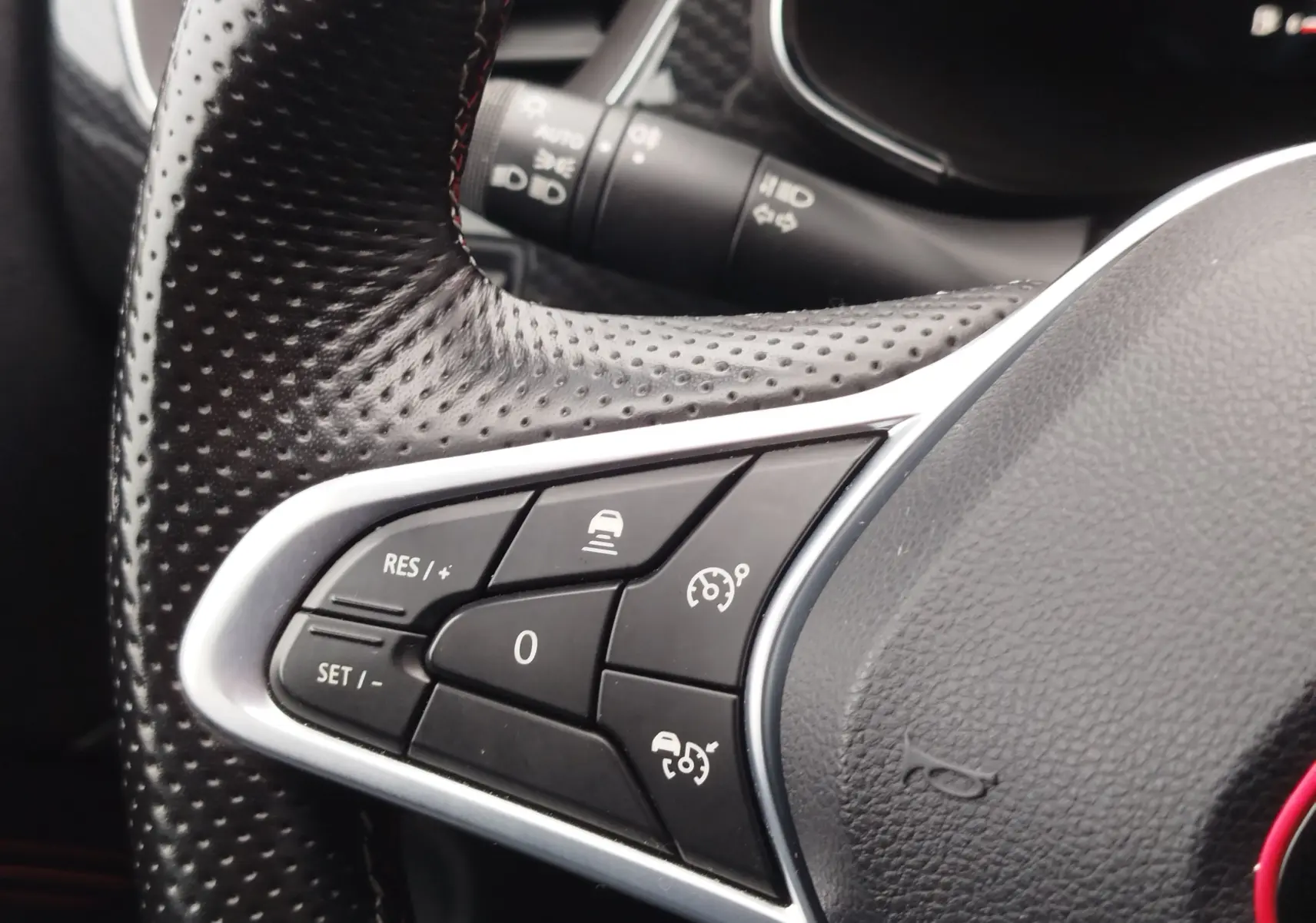 Gros plan sur les commandes de régulateur de vitesse au volant en cuir perforé noir du Renault Arkana bleu Zanzibar.