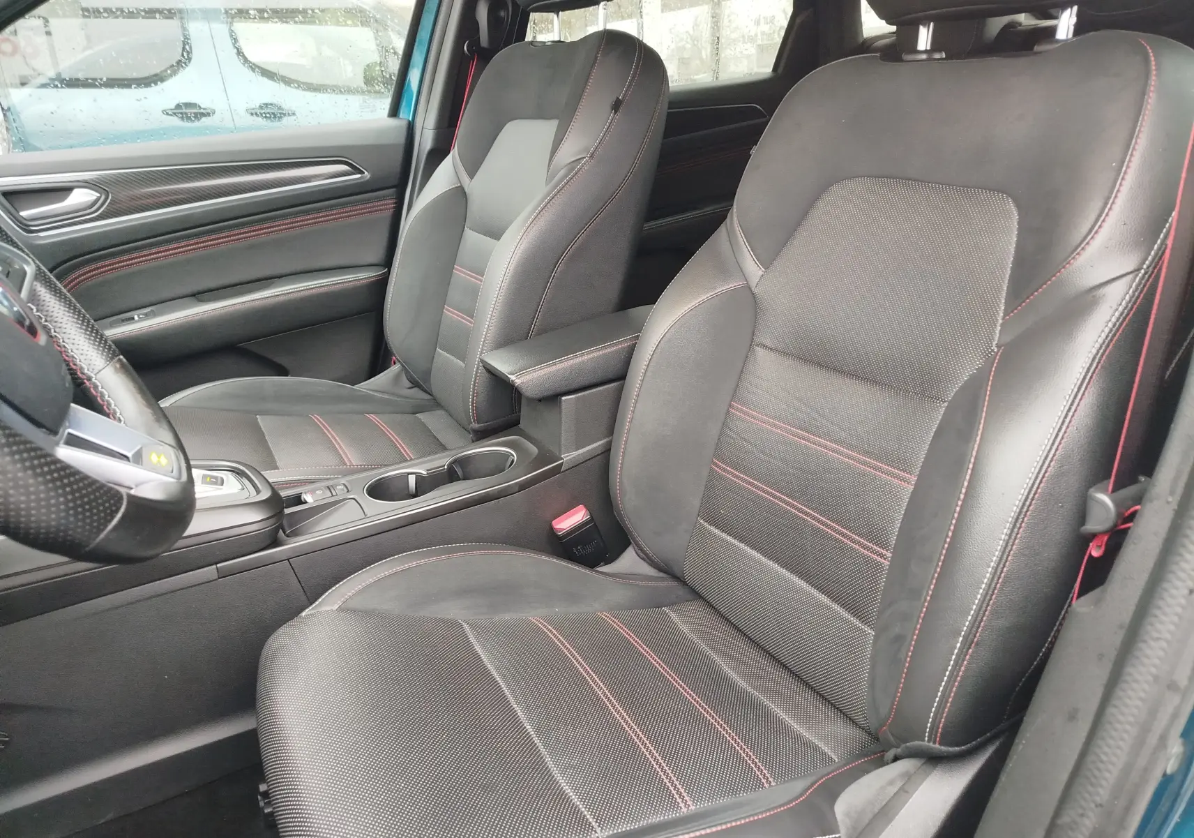 Vue intérieure côté conducteur du Renault Arkana bleu Zanzibar, sièges noirs en cuir et tissu avec surpiqûres rouges.