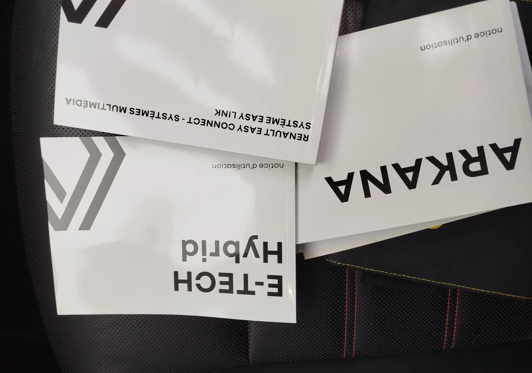 Manuels du Renault Arkana 1.6 E-Tech 145ch RS Line 2022 posés sur un siège noir avec surpiqûres rouges.