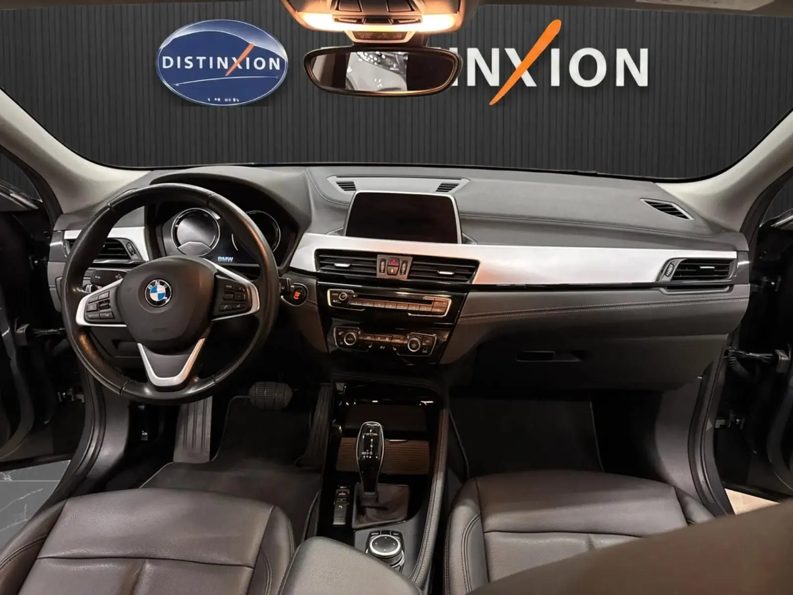 Vue intérieure avant du BMW X2 2019 montrant le tableau de bord noir, le volant cuir et la console centrale avec écran tactile.