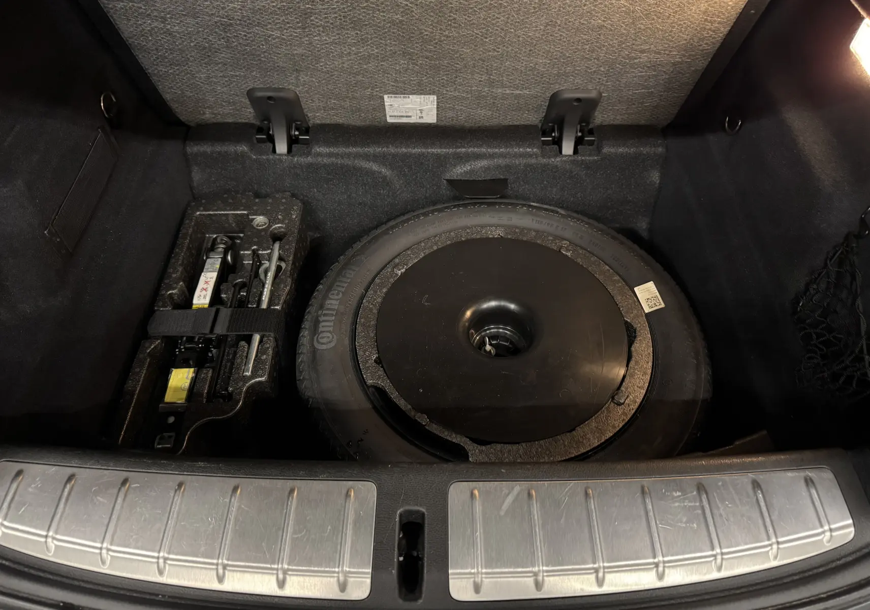 Coffre ouvert d’un BMW X2 gris Minéral Métallique montrant la roue de secours et le kit de réparation sous le plancher.