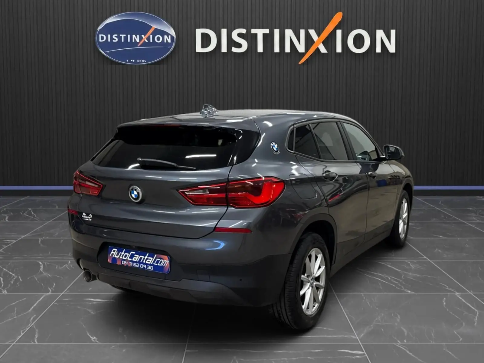 BMW X2 gris minéral métallisé vue 3/4 arrière droit, vitres surteintées et hayon fermé dans showroom.
