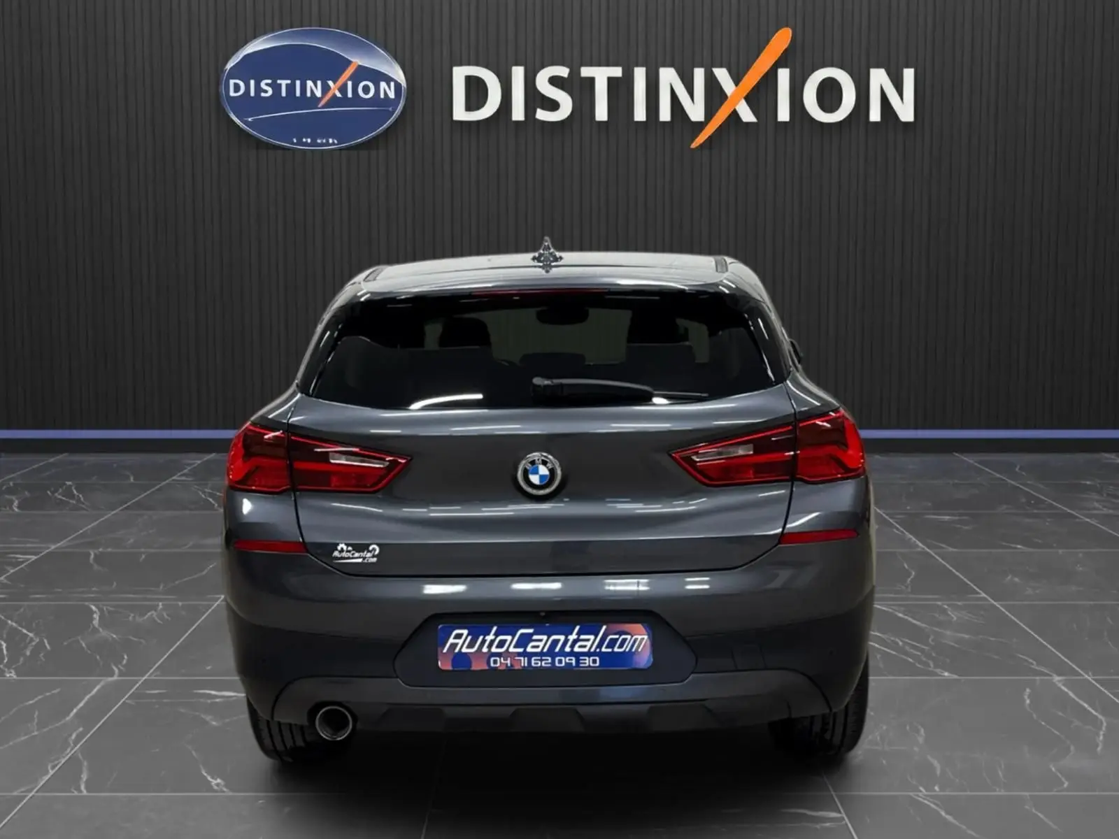 Vue arrière d'une BMW X2 gris minéral métallique 2019, avec hayon fermé et feux arrière allumés en intérieur showroom.