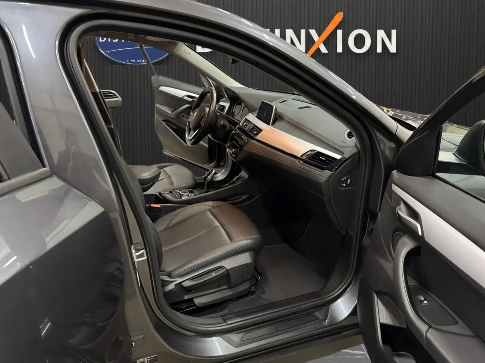 Vue intérieure côté conducteur d'une BMW X2 16dA Lounge Plus gris minéral métallique avec sièges cuir noir et tableau de bord moderne.