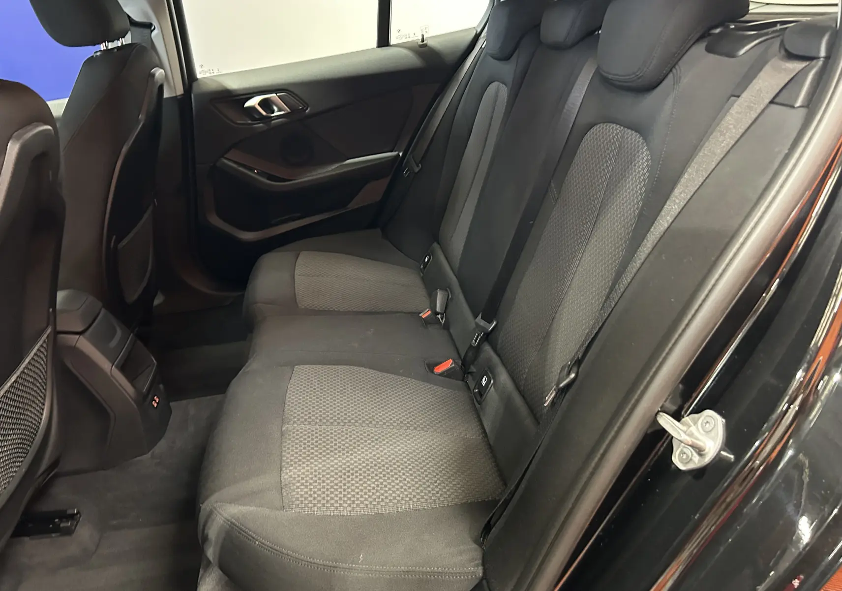 Vue intérieure côté droit des sièges arrière noirs en tissu de la BMW Série 1 16d 2023 avec porte ouverte.
