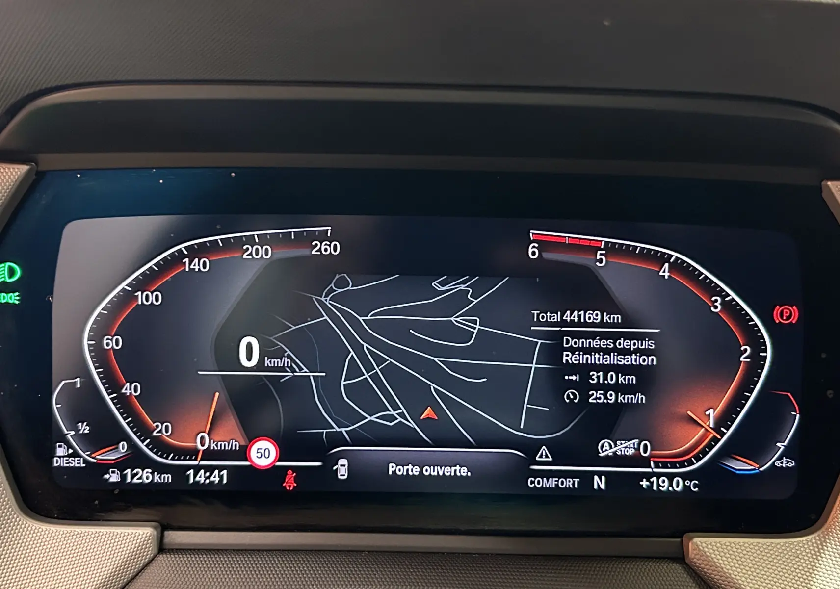 Tableau de bord numérique BMW Série 1 16d 2023 affichant vitesse, GPS et alertes, avec ambiance lumineuse rouge et orange.