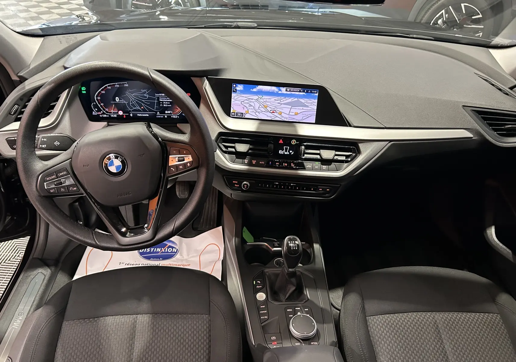 Intérieur BMW Série 1 16d 2023 en vue frontale, tableau de bord noir avec écran GPS et boîte manuelle visible.