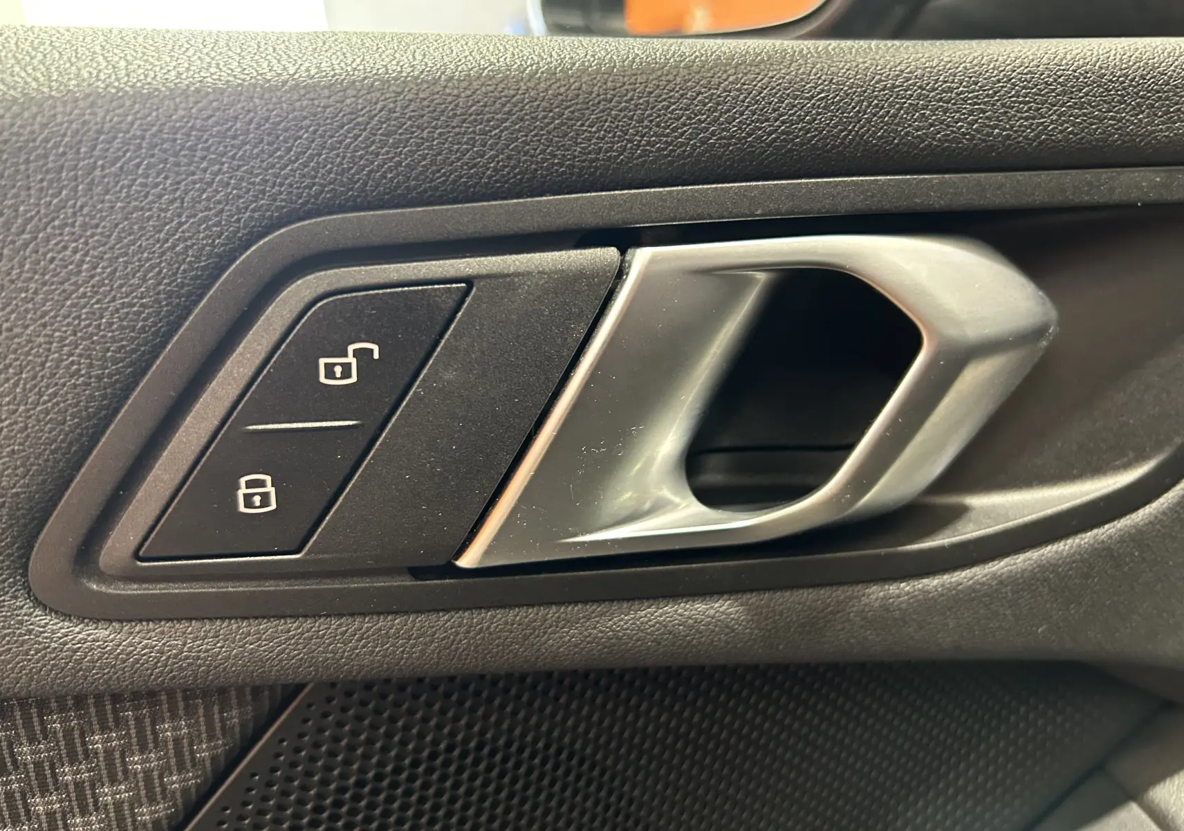 Poignée intérieure argentée et boutons de verrouillage sur la porte côté gauche d'une BMW Série 1 noire 2023.