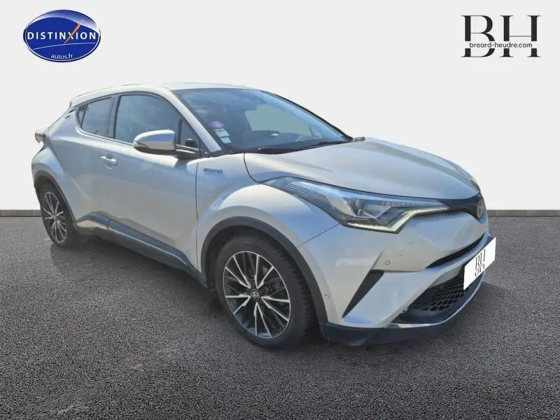 Vue 3/4 avant d'un Toyota C-HR 122h Distinctive gris aluminium avec jantes alliage et feux LED distinctifs.