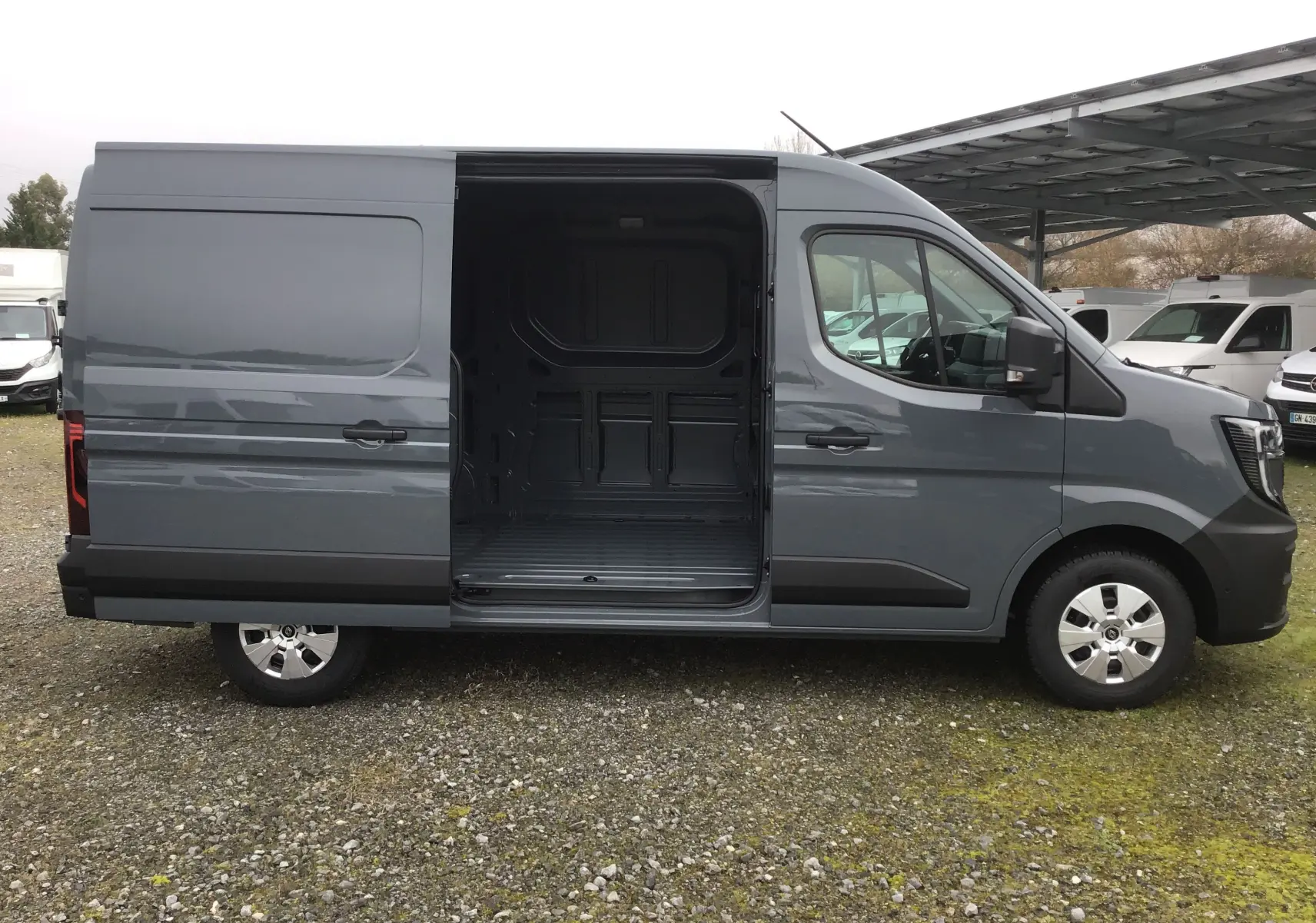 Vue latérale droite d’un Renault Master gris urbain 2025 avec porte coulissante ouverte montrant l’espace de chargement vide.