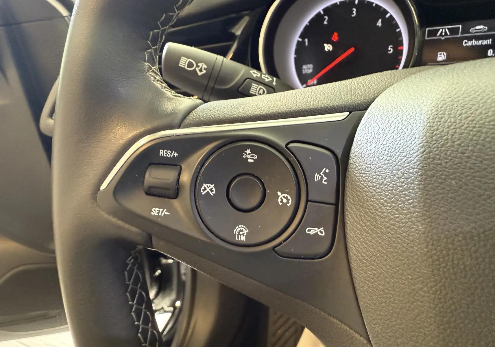 Gros plan sur les commandes du volant côté gauche de l'Opel Insignia Sports Tourer 2019, cuir noir et tableau de bord partiel.