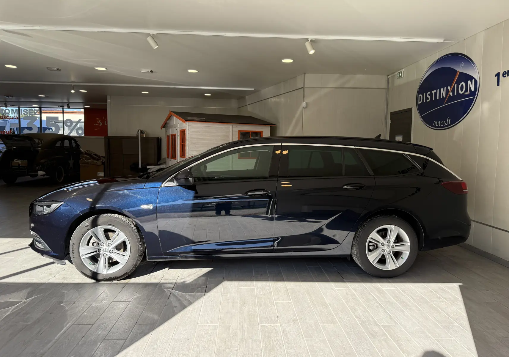 Profil côté gauche d'une Opel Insignia Sports Tourer bleu lune marine métal, en intérieur avec lumière naturelle soulignant sa silhouette élégante.
