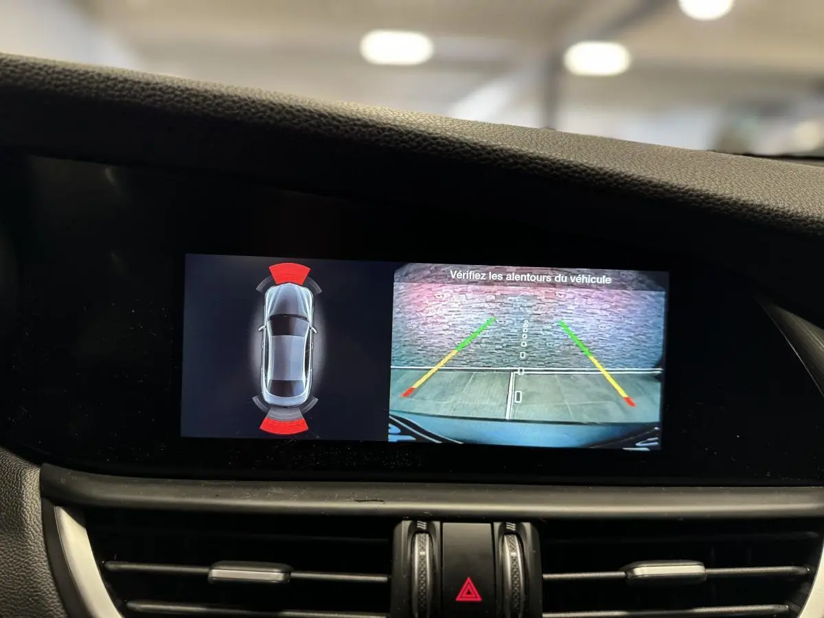 Écran intérieur de l'Alfa Romeo Giulia gris montrant la caméra de recul et l'aide au stationnement active.