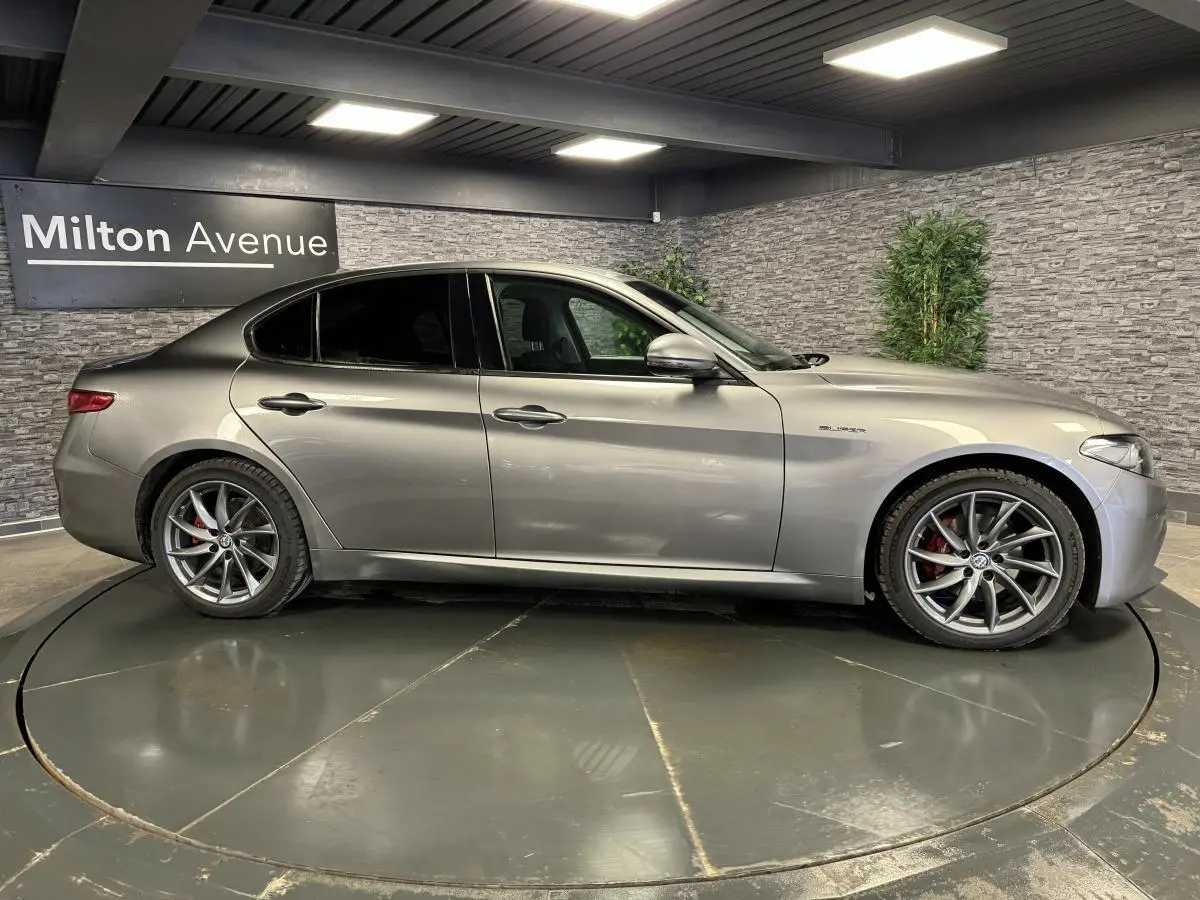 Vue latérale droite d'une Alfa Romeo Giulia gris métallisé avec jantes alliage 18 pouces Aero Scuro en intérieur showroom.