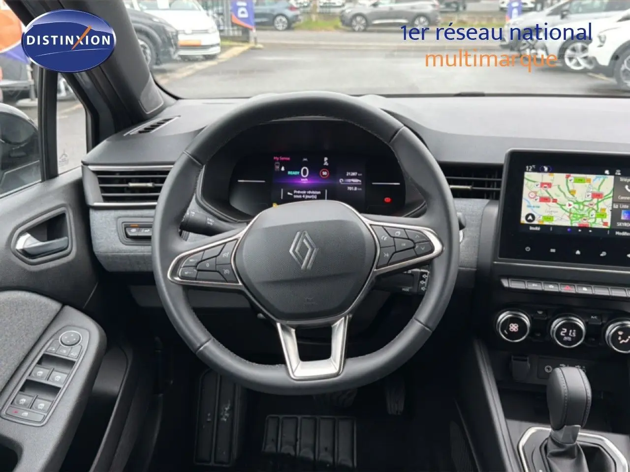 Vue intérieure centrée sur le volant et le tableau de bord de la Renault Clio gris Rafale, avec écran tactile et commandes visibles.
