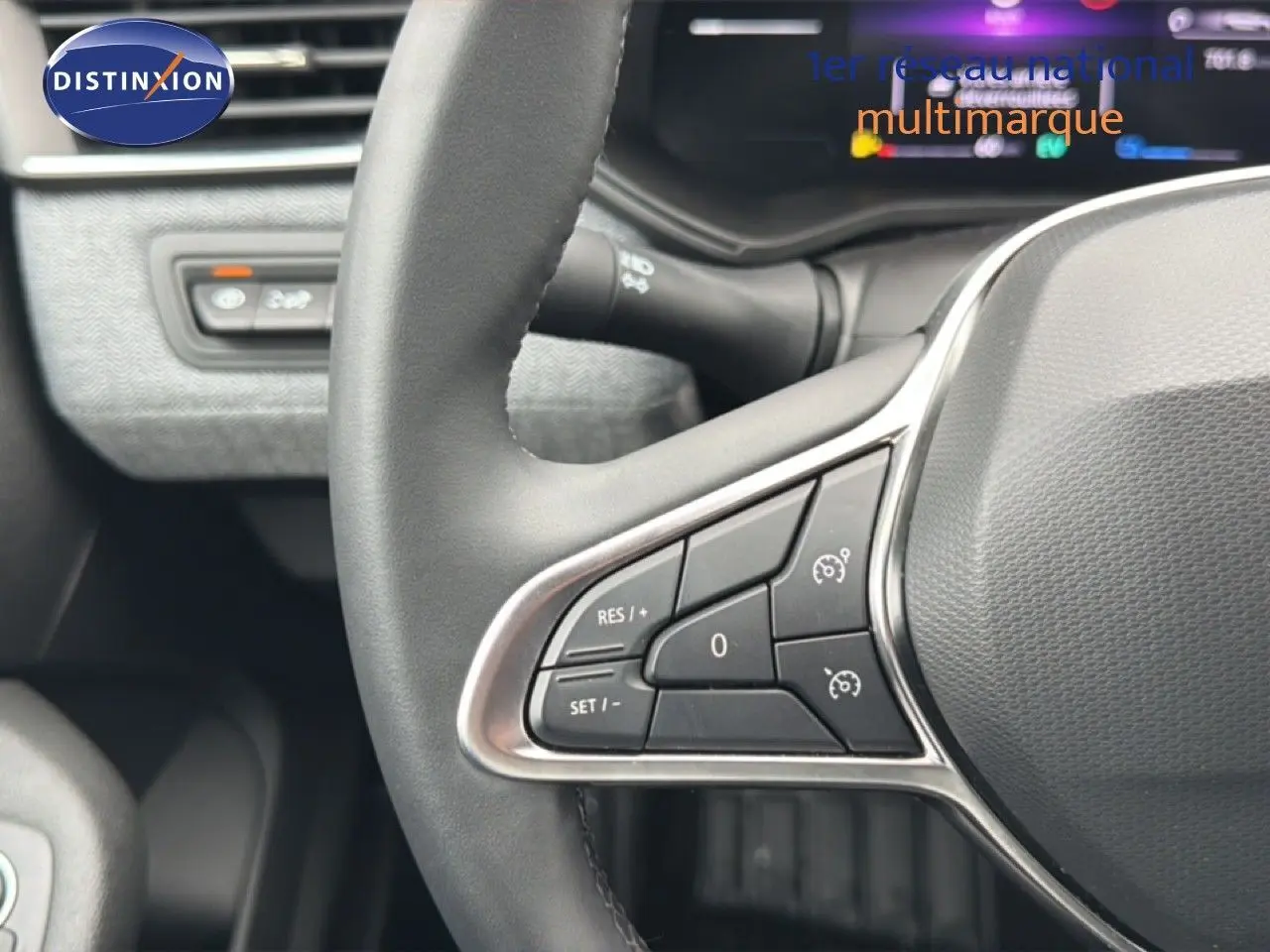 Gros plan sur le volant à droite de la Renault Clio 2025 gris Rafale Metal, avec commandes intégrées et tableau de bord flou en arrière-plan.