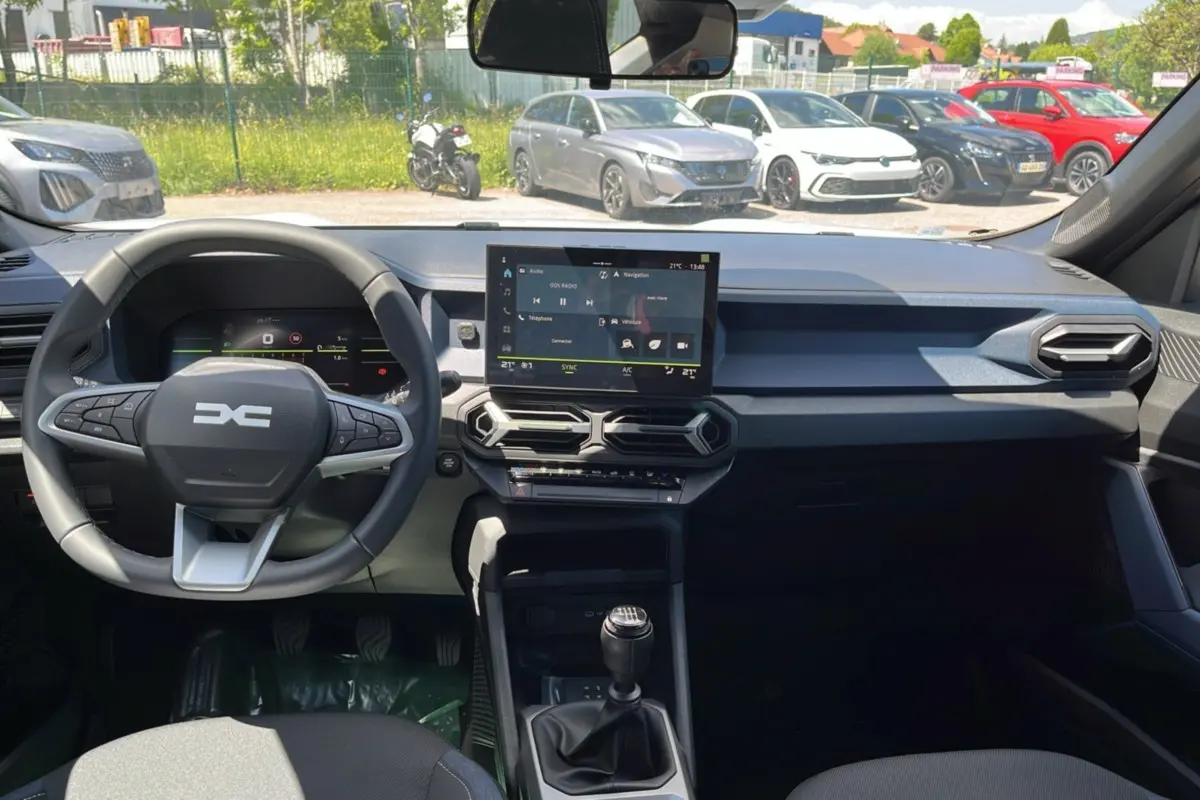Vue intérieure avant du tableau de bord et volant cuir du Dacia Bigster blanc glacier avec écran tactile et boîte manuelle.