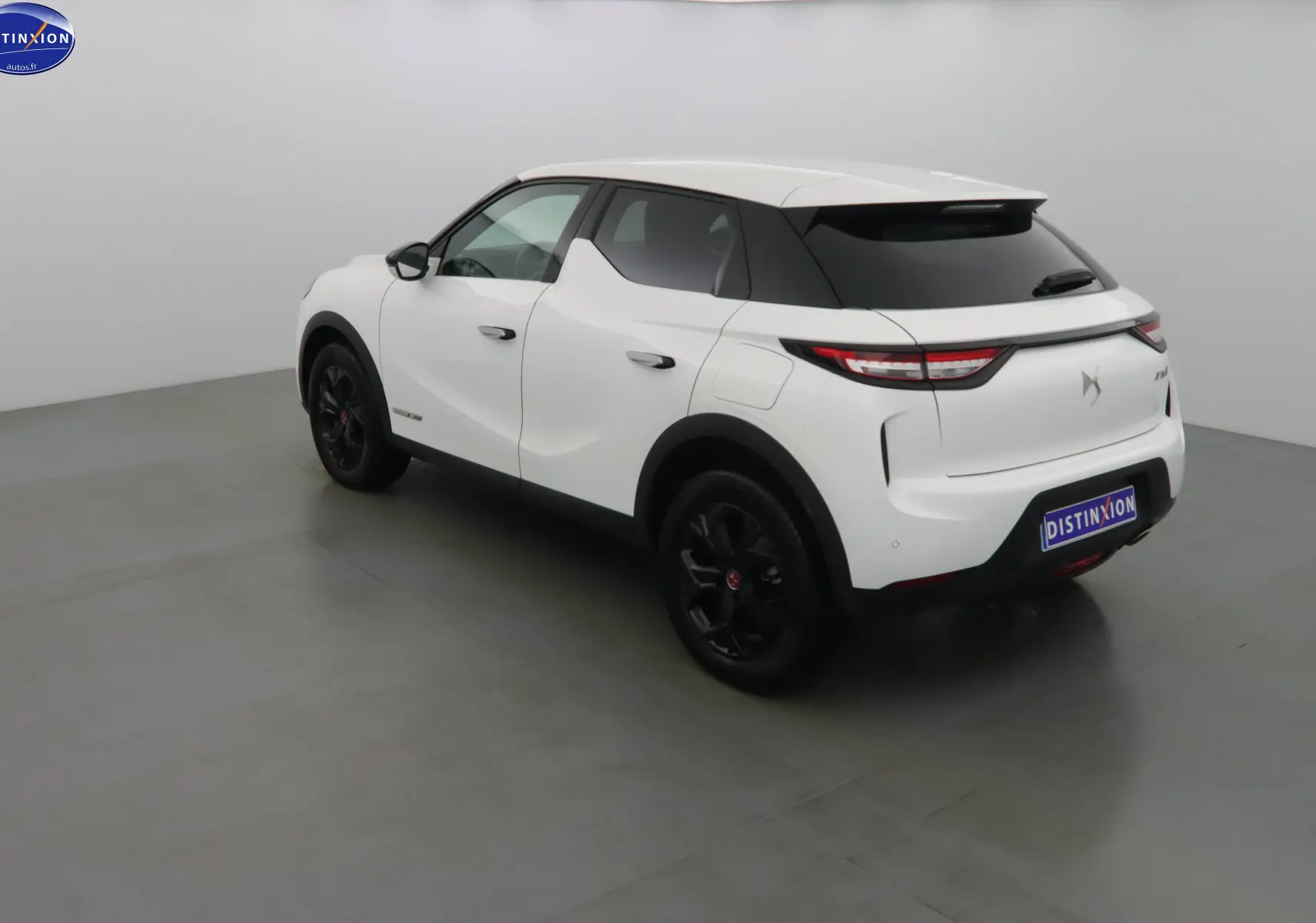Vue 3/4 arrière droite d'un DS3 Crossback blanc banquise avec jantes noires et toit noir contrasté.