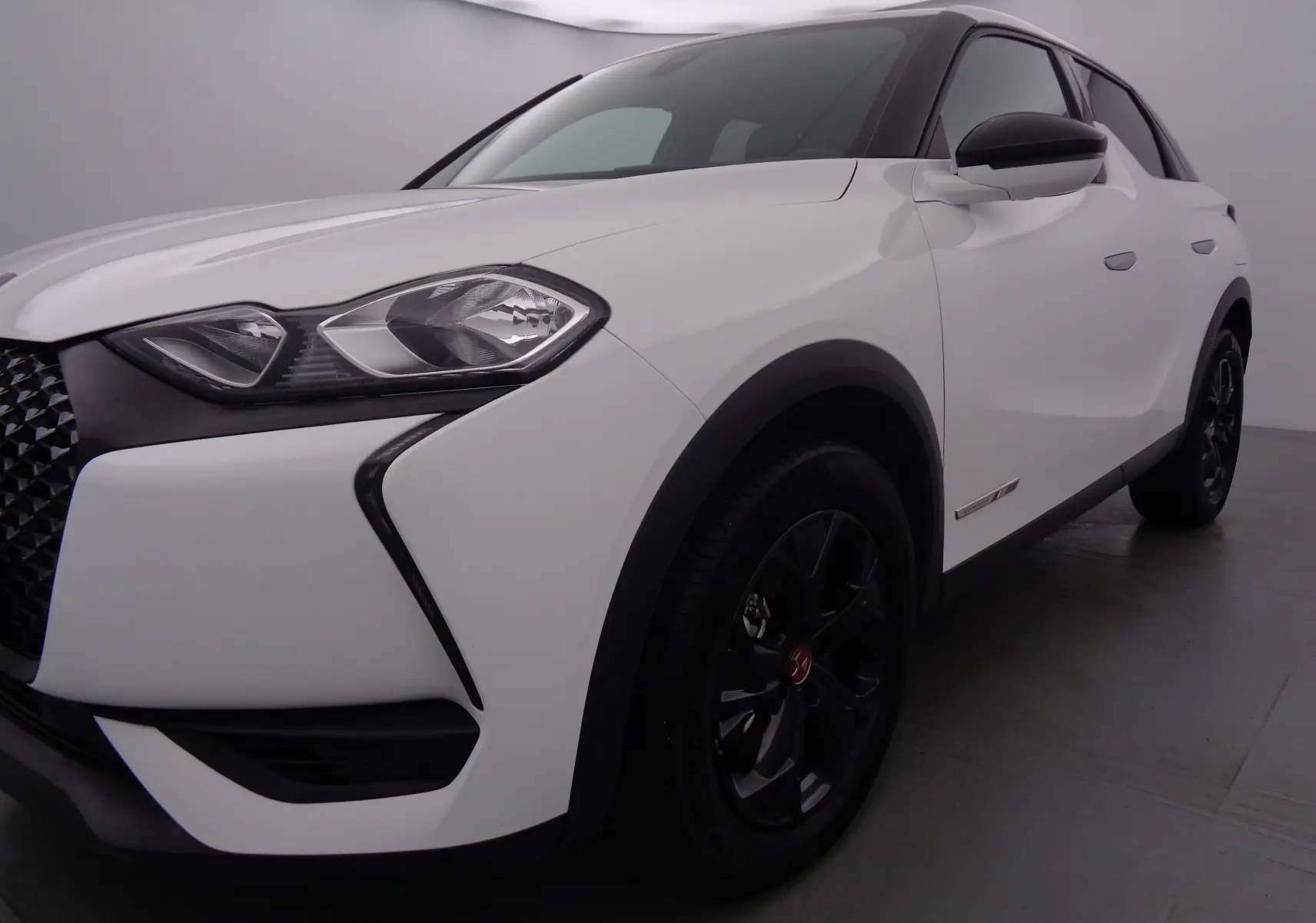 Vue 3/4 avant droit d'un DS3 Crossback blanc banquise avec jantes noires et détails noirs contrastants.