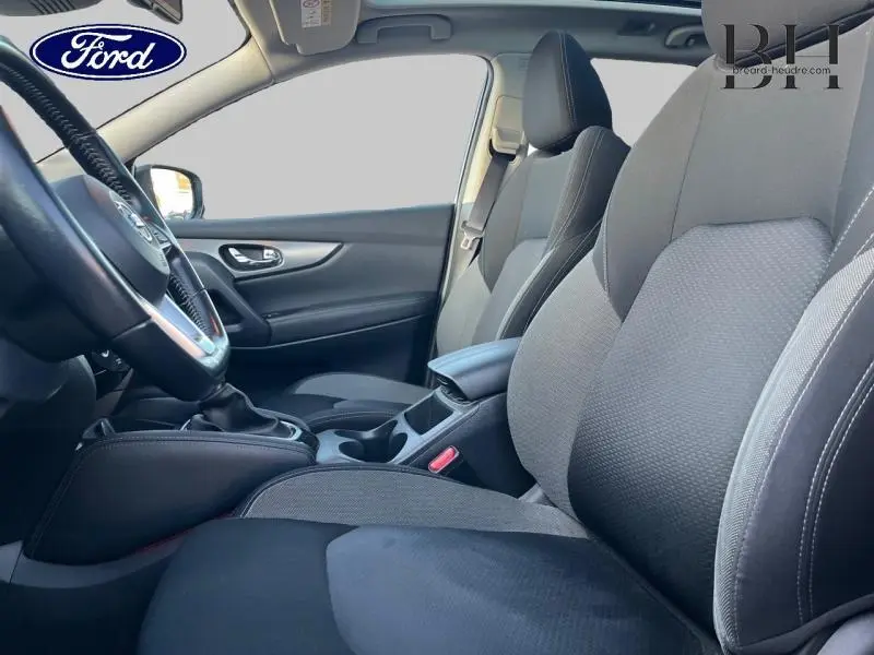 Intérieur avant du Nissan Qashqai 2019, sièges tissu gris, accoudoir central et volant multifonction visible côté conducteur.