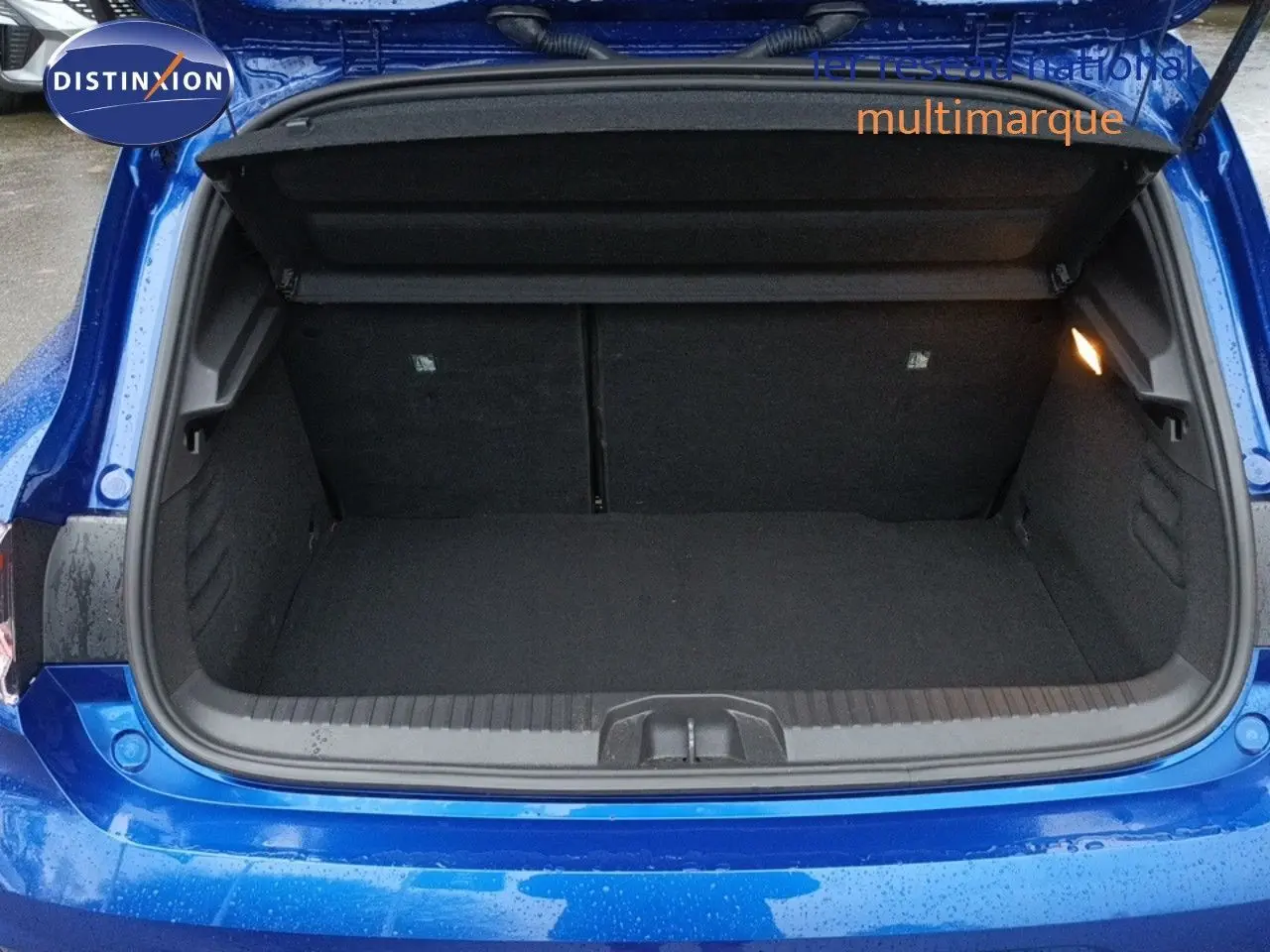 Coffre ouvert vu de l'arrière d'une Renault Clio 1.6 E-TECH bleu Iron Metal, intérieur noir et éclairage latéral.