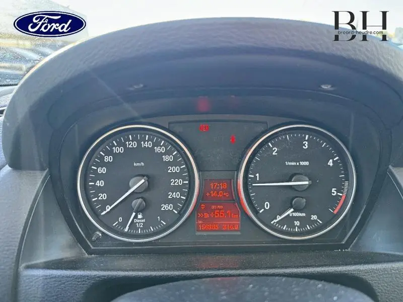 Vue rapprochée du tableau de bord BMW X1 Mineralgrau 2013, affichant compteur vitesse, compte-tours et écran multifonction rouge.