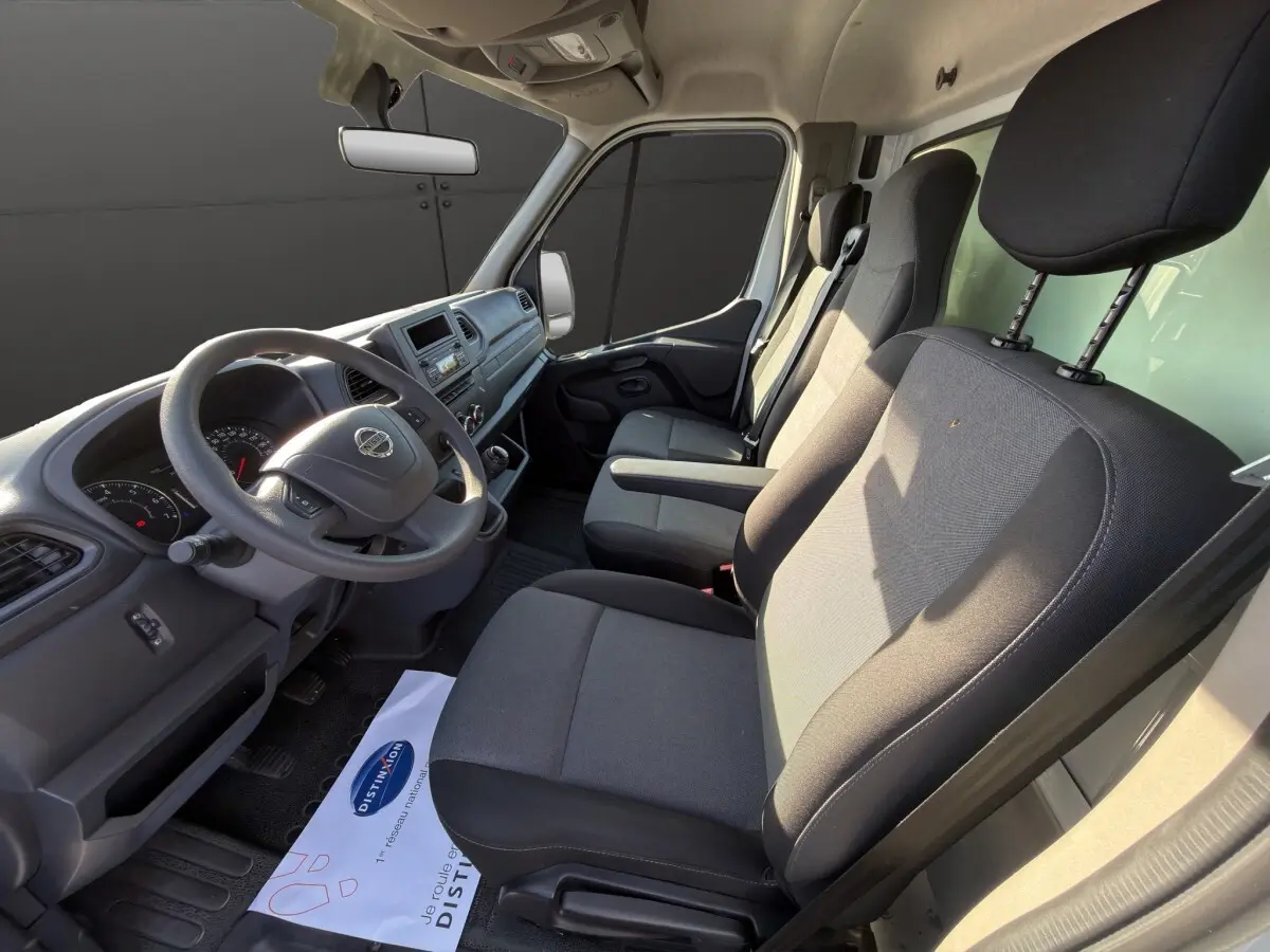 Vue intérieure côté conducteur du Nissan Interstar 2024, sièges gris et tableau de bord avec volant multifonctions.
