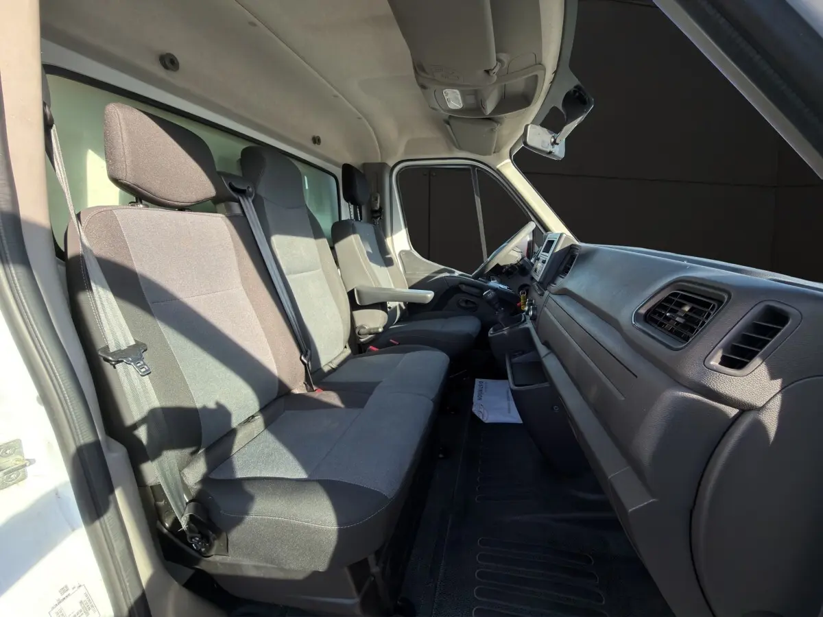 Vue intérieure côté conducteur du Nissan Interstar 2024 blanc, montrant les sièges gris et le tableau de bord noir.