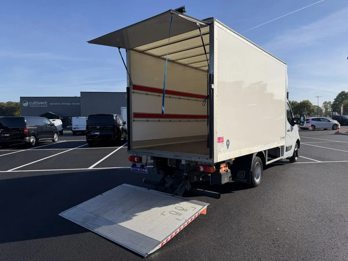 Nissan Interstar blanc vu 3/4 arrière avec hayon élévateur déployé et caisse ouverte sur parking.