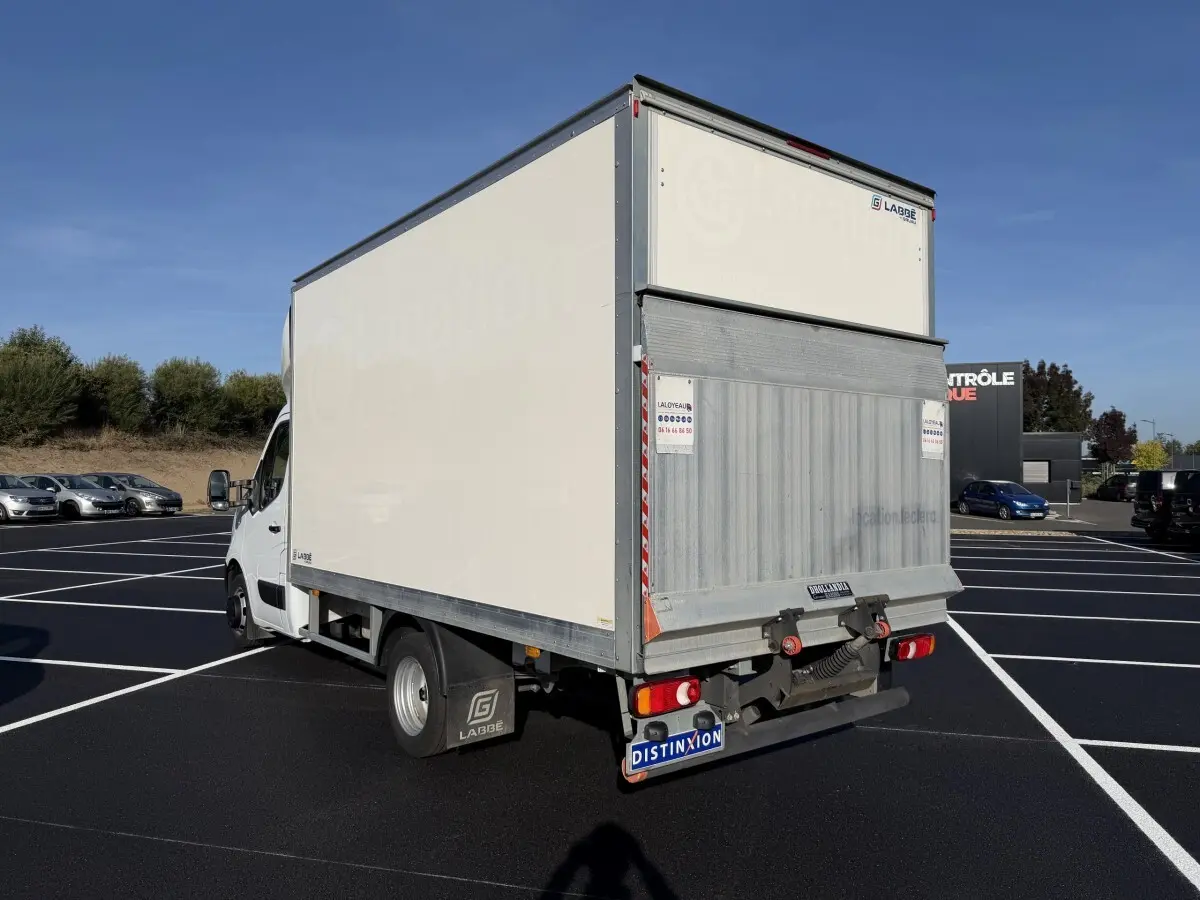 Vue 3/4 arrière droite d’un utilitaire blanc Nissan Interstar avec caisse fermée et hayon métallique en parking.