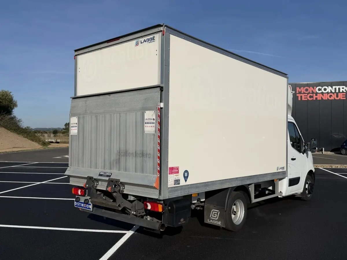 Vue 3/4 arrière droite d’un utilitaire blanc Nissan Interstar avec caisse fermée et hayon élévateur, stationné sur un parking.