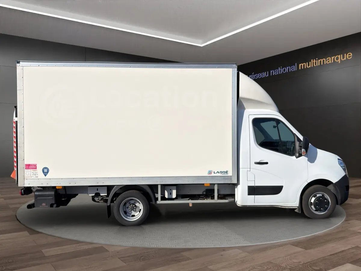 Vue latérale droite d’un utilitaire blanc Nissan Interstar avec caisse fermée et hayon, en intérieur showroom.