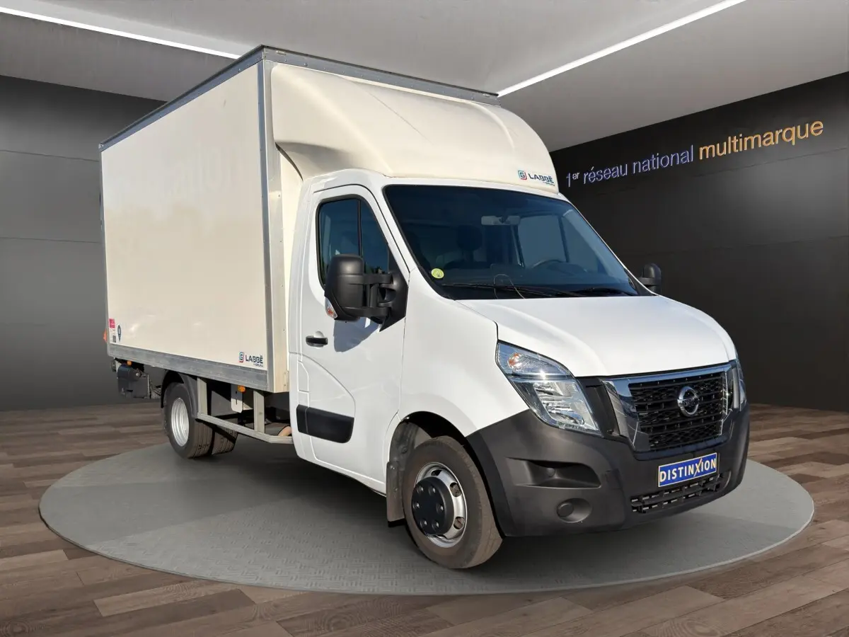 Vue 3/4 avant droit d’un utilitaire blanc Nissan Interstar avec caisse de livraison et hayon, sur fond neutre intérieur.