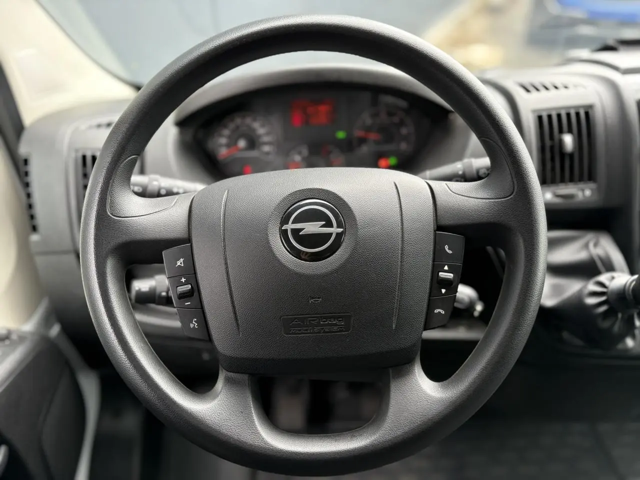 Volant noir avec logo Opel au centre, vue rapprochée de l'intérieur du Movano Fourgon 2023, tableau de bord flou en arrière-plan.