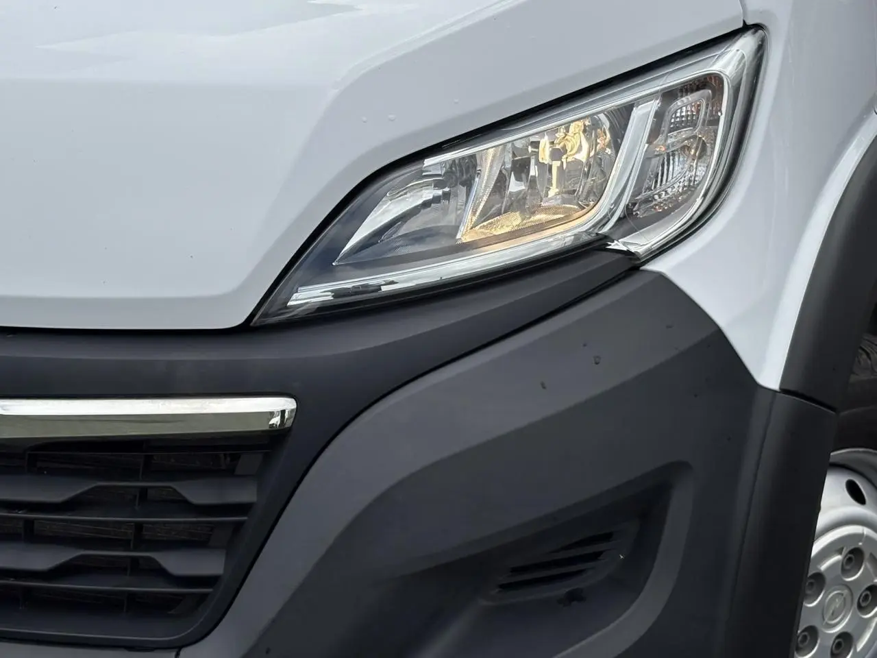 Gros plan sur le phare avant droit blanc de l'Opel Movano Fourgon 2023 avec calandre noire et jante acier visible.