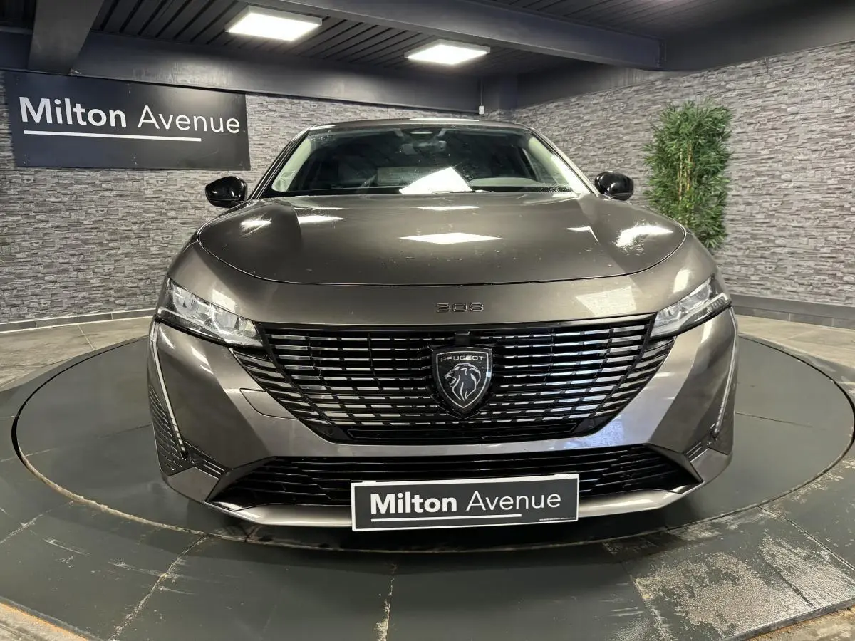 Vue frontale d'une Peugeot 308 SW gris métallisé avec calandre noire et logo lion central lumineux.