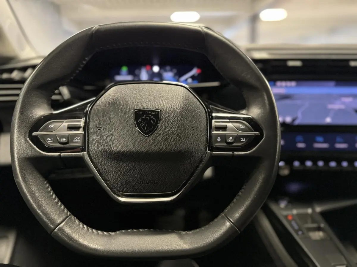 Volant cuir noir Peugeot 308 SW 2022 vu de face avec tableau de bord numérique et écran tactile bleu en arrière-plan.