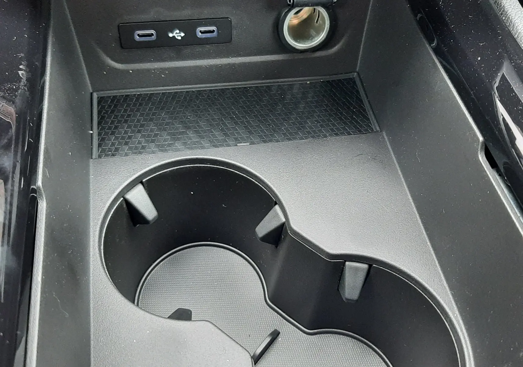 Gros plan sur la console centrale noire du Renault Austral Ph.2 avec porte-gobelets, prises USB et allume-cigare.