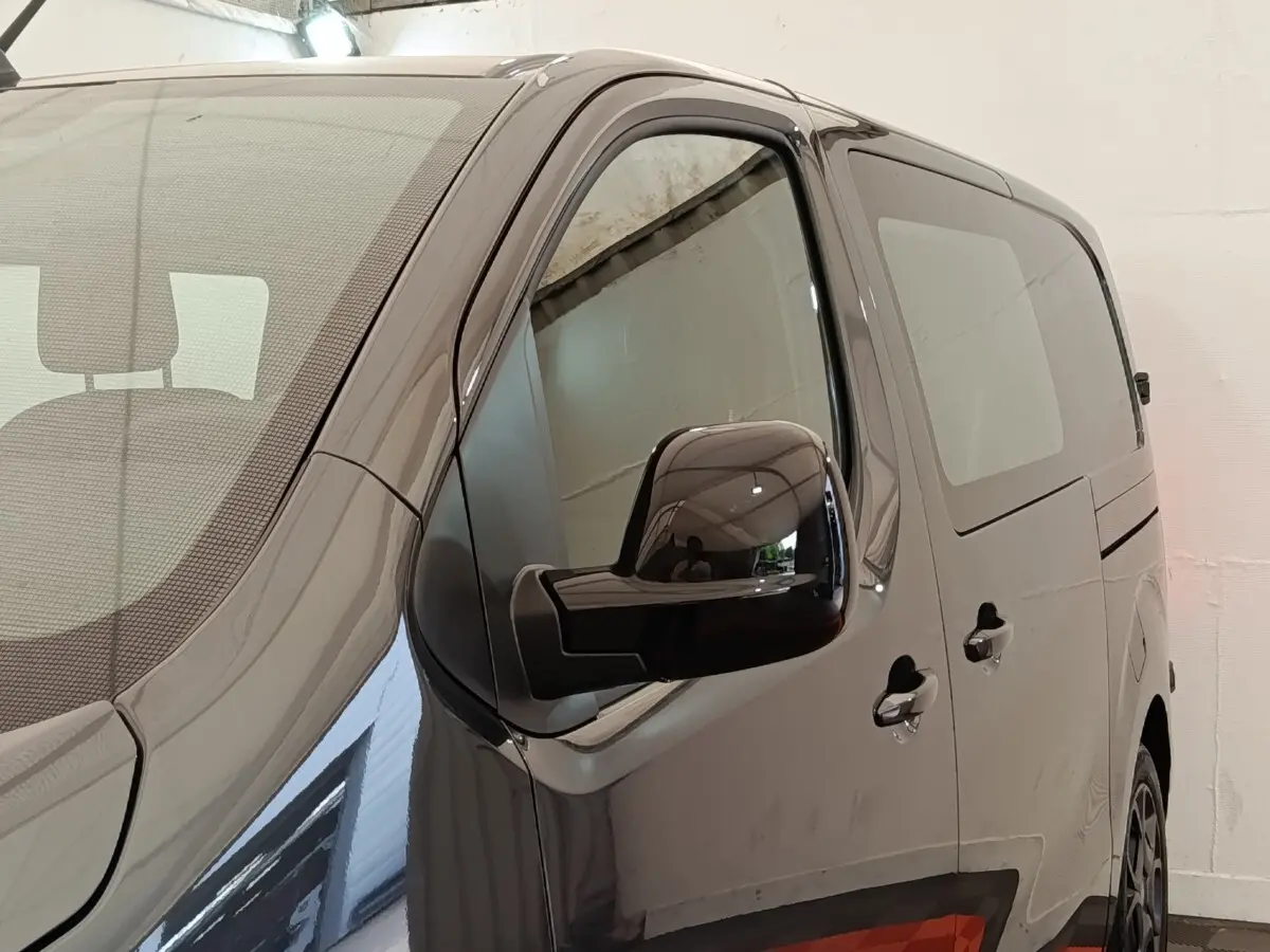 Vue de côté droit avant d’un Citroën Jumpy gris foncé avec vitres teintées et rétroviseur noir brillant.