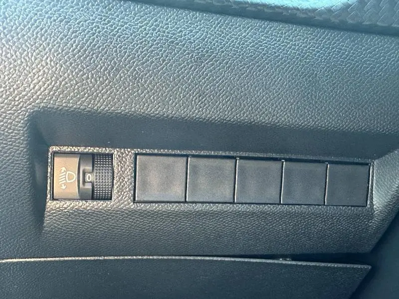 Gros plan sur le réglage des phares et les emplacements de boutons vides sur le tableau de bord noir d'une Peugeot 208 2024.