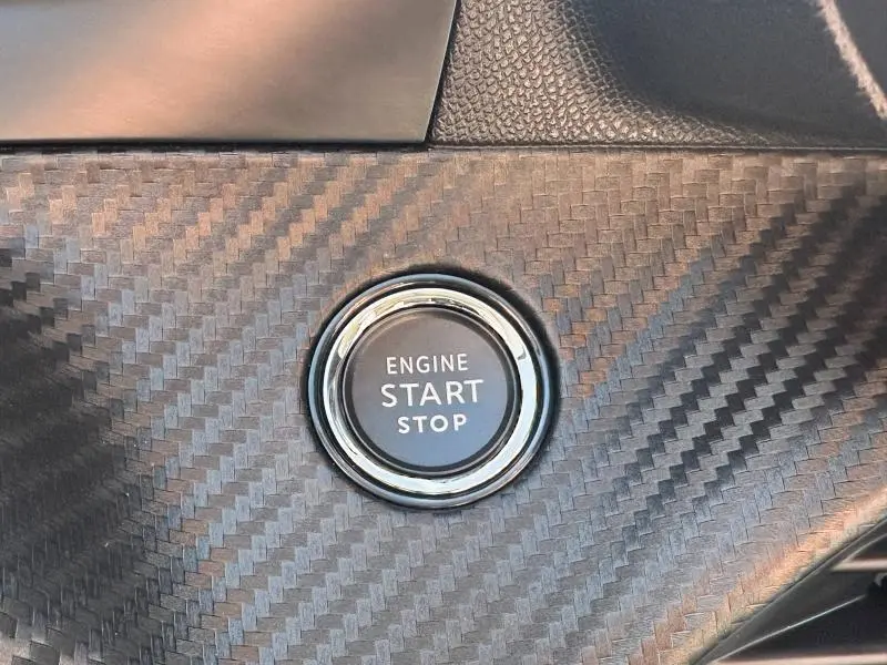 Bouton moteur start/stop en gros plan sur tableau de bord à finition carbone d'une Peugeot 208 gris 2024.
