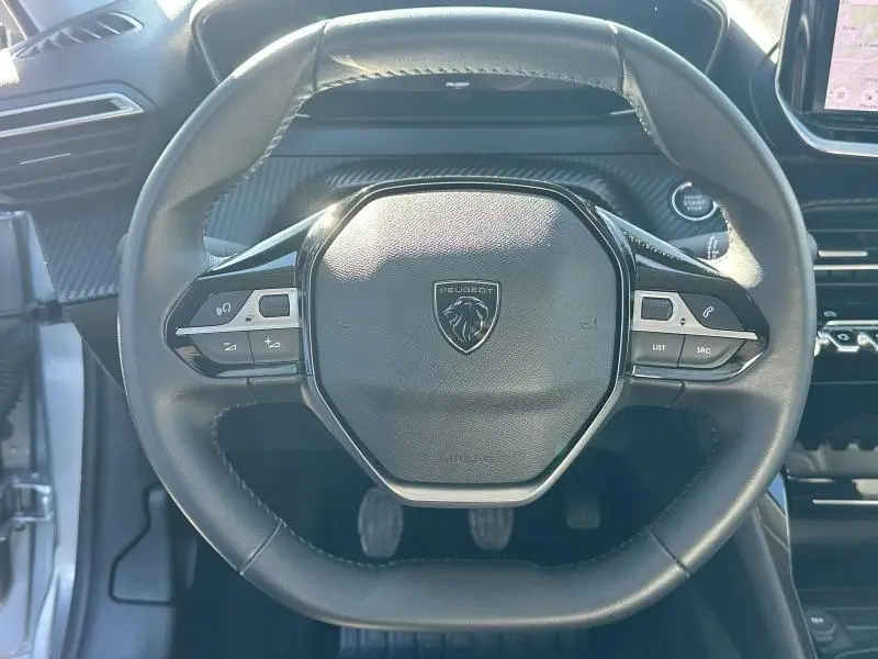 Volant cuir noir de Peugeot 208 1.2 100ch Allure 2024 avec commandes intégrées et logo lion au centre.