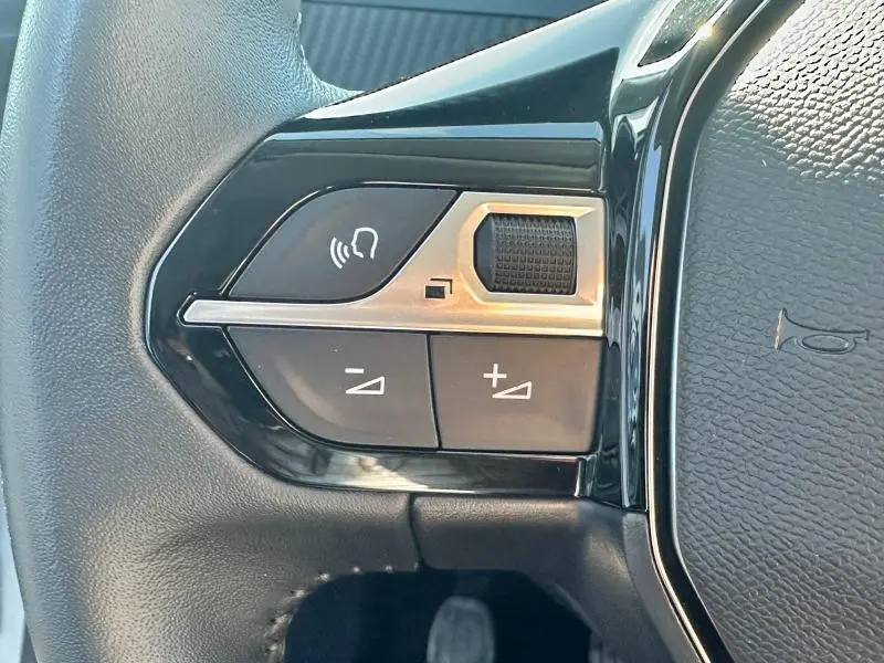 Gros plan sur les commandes de volume et de téléphone intégrées au volant cuir noir du Peugeot 208 gris 2024.