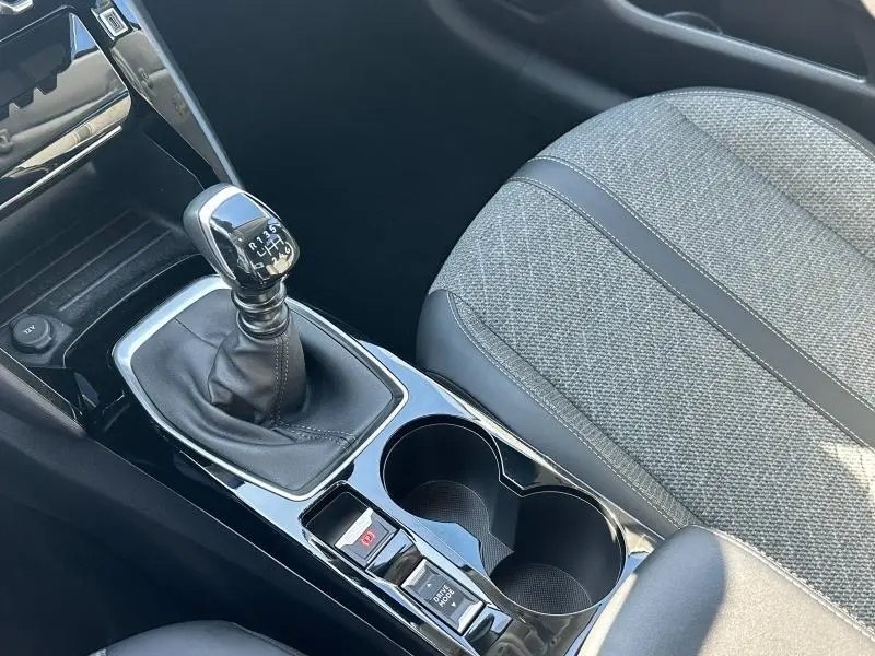 Gros plan sur la console centrale d'une Peugeot 208 2024 gris, montrant la boîte manuelle et les porte-gobelets côté droit du siège passager.