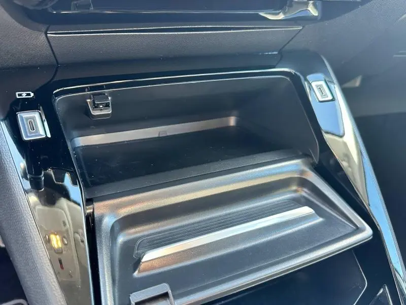 Détail de la console centrale noire brillante du Peugeot 208 1.2 100ch S&S Allure 2024 avec espace de rangement ouvert.