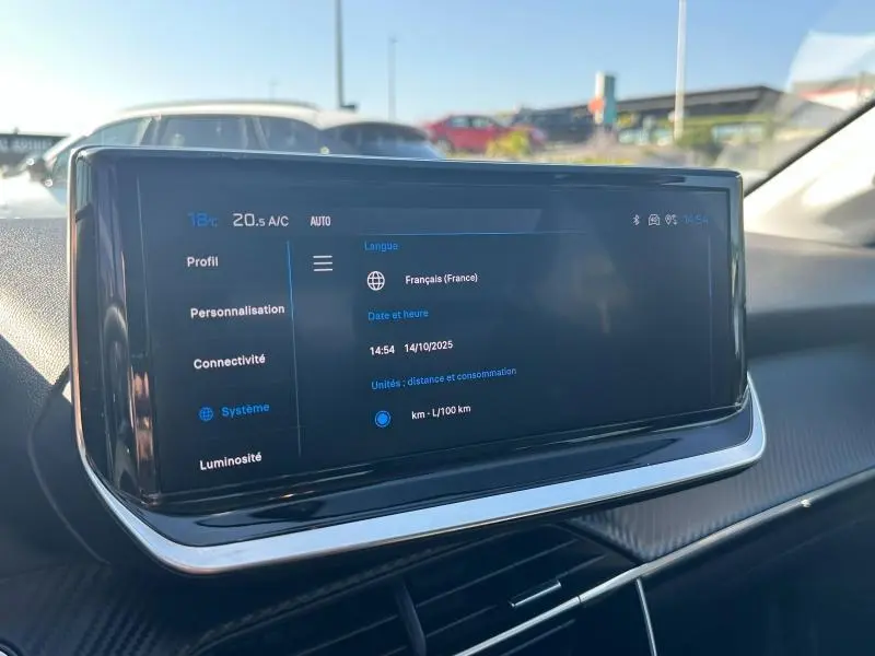 Écran tactile central du tableau de bord de la Peugeot 208 2024, affichant les réglages système en intérieur lumineux.