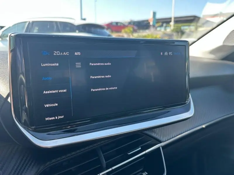 Écran tactile central du tableau de bord de la Peugeot 208 gris 2024, affichant les paramètres audio et climatisation.